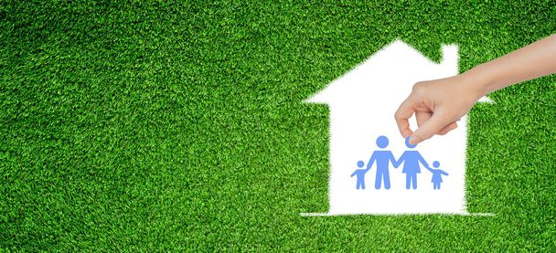 Conceito de família feliz: Mão Segurando e colocando ícones da família em casa branca na grama artificial verde arquivado
. - Foto, Imagem