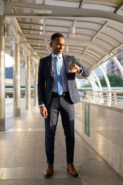 Portrait of young handsome African businessman wearing suit at skywalk bridge in the city - Valokuva, kuva