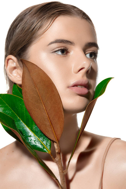 Youth. Close up of beautiful young woman with green leaves on her face over white background. Cosmetics and makeup, natural and eco treatment, skin care - Фото, зображення