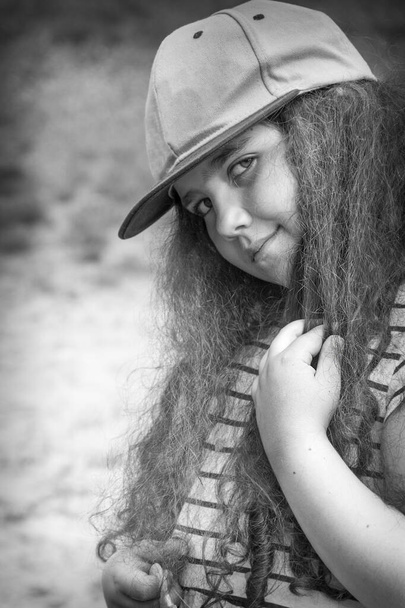 In summer, in the park, a little curly girl in a cap .Black and white photo. Close-up. - Photo, Image