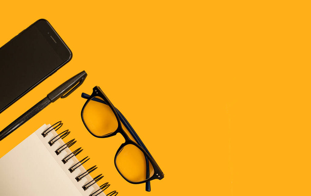 Elrendezés notebook toll telefon szemüveg sárga háttérrel. Első látásra. Lapos fektetés - Fotó, kép