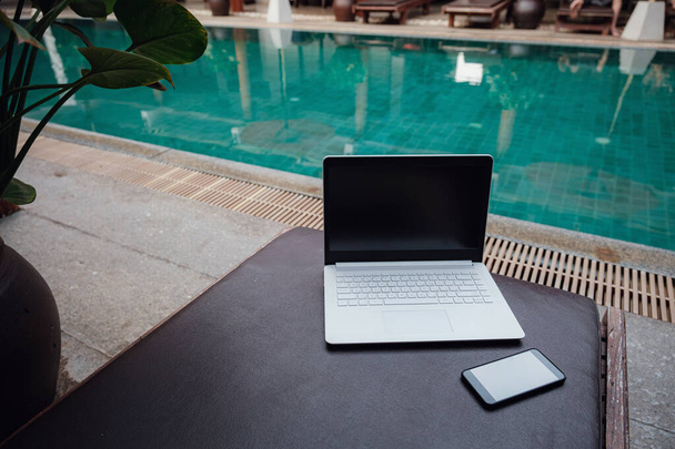 Ordenador portátil blanco en la piscina y el smartphone, espacio de trabajo en un freelancer de vacaciones
. - Foto, Imagen