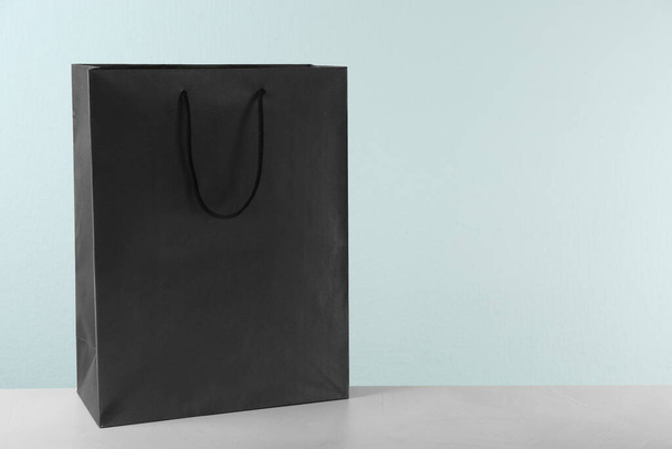 Black shopping paper bag on table against light background. Space for text - Valokuva, kuva