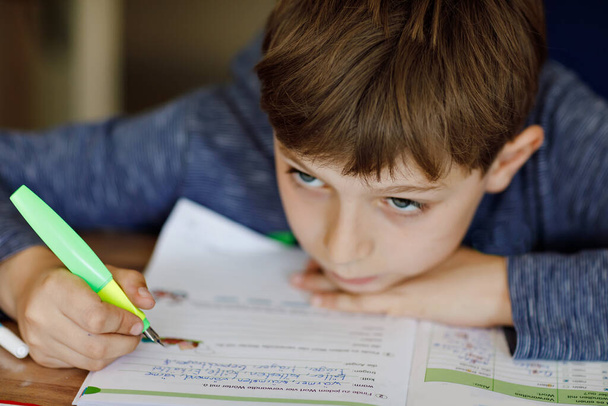 コロナ大流行病からの隔離期間中に宿題をしている未就学児の少年。疲れて悲しい少年は家にいるのをいらいらさせる。家庭教育の概念 - 写真・画像