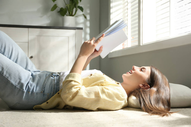 Beautiful young woman reading book at home - Фото, изображение