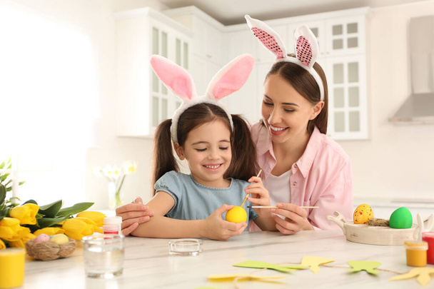 Happy mother and daughter with bunny ears headbands painting Easter egg in kitchen - Foto, immagini