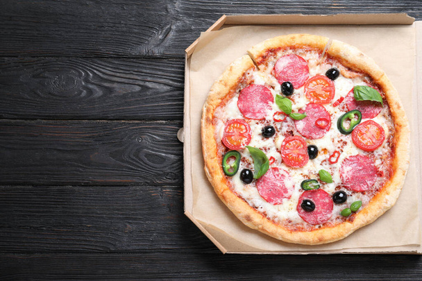 Delicious pizza Diablo in cardboard box on wooden background, top view. Space for text - Foto, Imagen