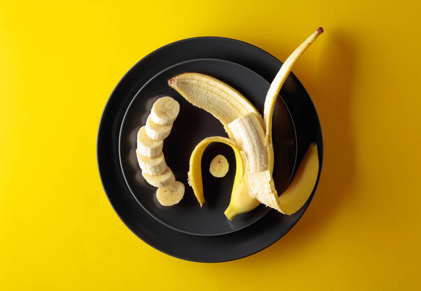 Ripe juicy banana on a black plate. Top view, copy space. - Photo, Image