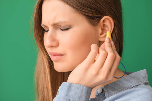 Young woman with ear plugs on color background - Photo, Image