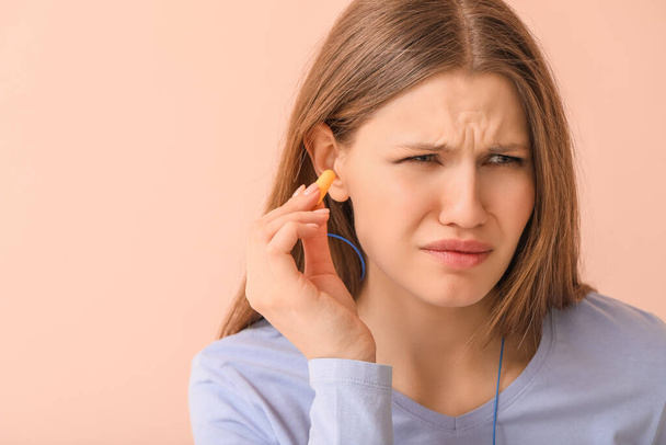 Young woman with ear plugs suffering from loud noise on color background - Photo, Image