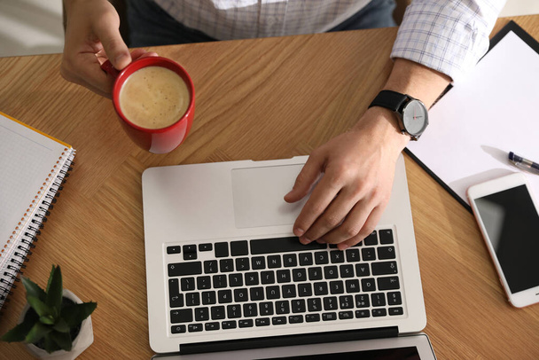 İş yerinde bir fincan kahve ve dizüstü bilgisayarı olan bir adam. - Fotoğraf, Görsel