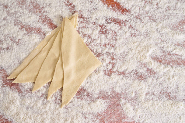 Des morceaux de pâte savoureuse prête à l'emploi couchés sur une table de cuisine en bois couverte de farine vue du dessus
 - Photo, image
