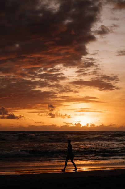 CANGGU, BALI, INDONESIA - 25 FEBBRAIO 2019: Surfista di sesso maschile passeggia lungo la riva del mare tenendo la sua tavola da surf al tramonto estivo sulla costa di Bali. Attività ricreative e sport acquatici durante le vacanze in Indonesia
 - Foto, immagini