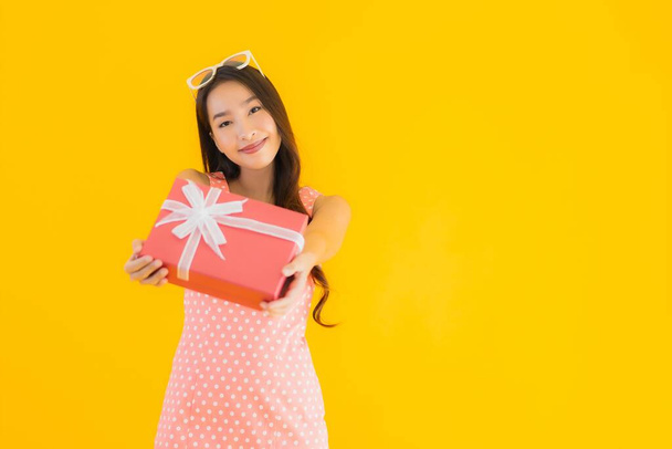 Portrait beautiful young asian woman with red gift box on yellow isolated background - Photo, Image