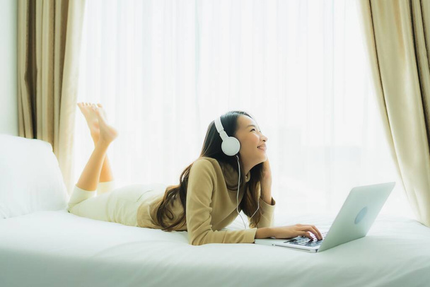 Młoda azjatycka kobieta przy użyciu laptopa ze słuchawką do słuchania muzyki we wnętrzu sypialni - Zdjęcie, obraz