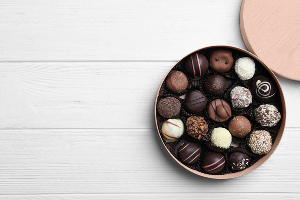 Box with tasty chocolate candies on white wooden table, flat lay. Space for text - Fotoğraf, Görsel