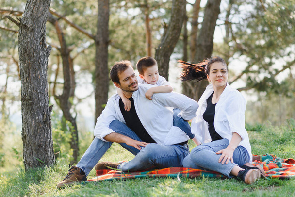 szczęśliwa młoda rodzina spędza czas na świeżym powietrzu w letni dzień bawić się w pięknym parku w przyrodzie siedząc na zielonej trawie. Szczęśliwa rodzina. - Zdjęcie, obraz