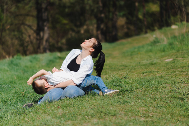 Happy young mother is playing with her baby in a park on a green lawn. Happiness and harmony of family life. Great family vacation. Good weekend. Mothers Day. Holiday. The concept of a happy family. - Φωτογραφία, εικόνα
