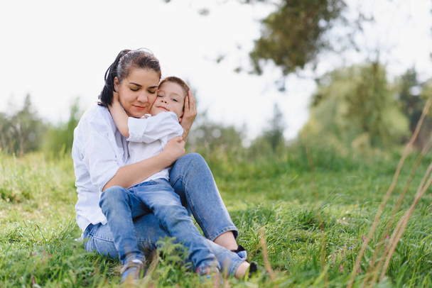 Gelukkige jonge moeder speelt met haar baby in een park op een groen grasveld. Geluk en harmonie in het gezinsleven. Geweldige familievakantie. Goed weekend. Moederdag. Vakantie. Het concept van een gelukkig gezin. - Foto, afbeelding