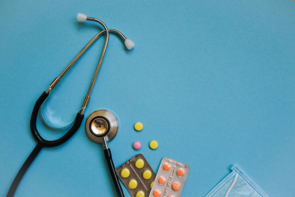 Stethoscope, pills and mask on blue background. - Photo, Image