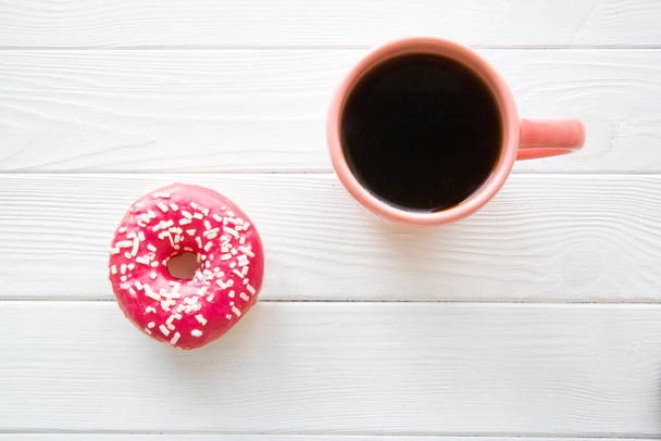 A cup of black coffee and sparkling pink doughnut on white wooden table baclground. Space for text, copy space.  - Foto, Imagem