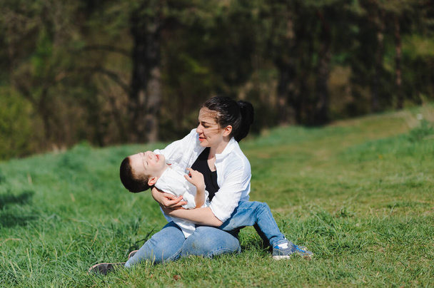 Gelukkige jonge moeder speelt met haar baby in een park op een groen grasveld. Geluk en harmonie in het gezinsleven. Geweldige familievakantie. Goed weekend. Moederdag. Vakantie. Het concept van een gelukkig gezin. - Foto, afbeelding