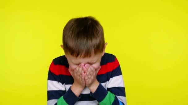 Sick little boy sneezes and covers his mouth with palms on a yellow background - Footage, Video