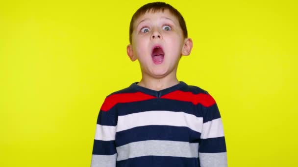Μικρό αγόρι σε ένα πολύχρωμο πουλόβερ είναι έκπληκτος σε ένα κίτρινο φόντο - Πλάνα, βίντεο