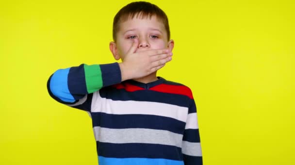 Μικρό αγόρι κάλυψε το στόμα του με την παλάμη του και στέκεται σε κίτρινο φόντο - Πλάνα, βίντεο