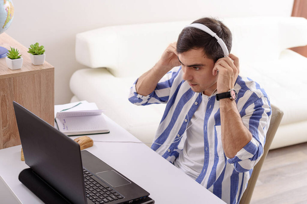 красивый мужчина брюнетка в полосатой рубашке слушать музыку с белыми наушниками, онлайн-курсы, домашняя концепция обучения
 - Фото, изображение
