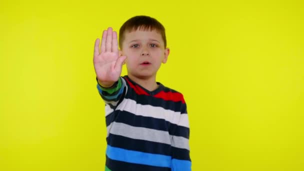 Niño serio levanta la mano con la palma y dice DETENER sobre un fondo amarillo - Metraje, vídeo