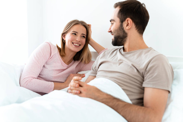 Portrait of young happy couple smiling and looking at each other while lying at home bedroom - Foto, Bild