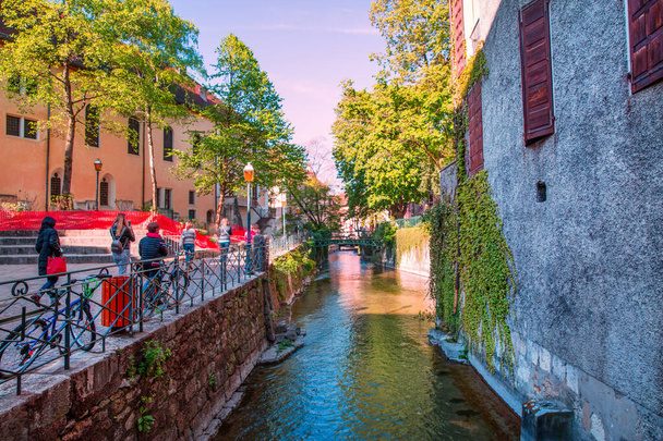 Annecy jasne kolory, Francja. Turyści przechodzą przez ulicę w pobliżu zielonego kanału.   - Zdjęcie, obraz