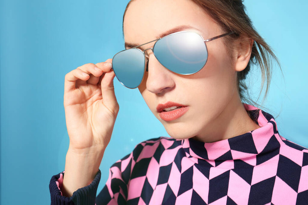 Young woman wearing stylish sunglasses on blue background - Фото, зображення