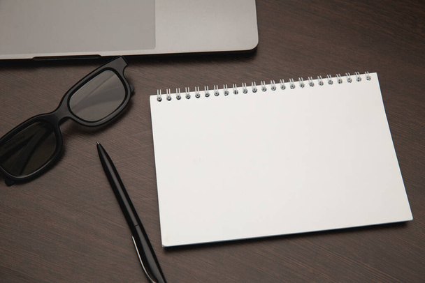 Business-Arbeitsplatz mit Notizblock, Laptop, Stift und Brille auf Holztisch - Foto, Bild