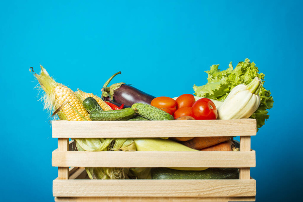 Holzkiste mit frischem Gemüse auf blauem Hintergrund. Gutes Erntekonzept, Naturprodukt. - Foto, Bild