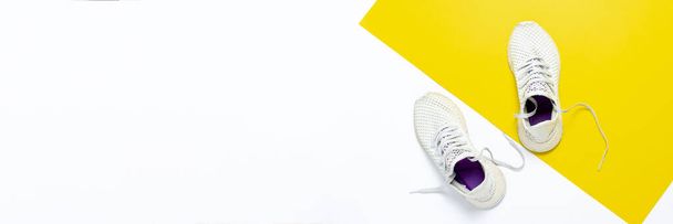 Λευκά αθλητικά παπούτσια σε ένα αφηρημένο κίτρινο-λευκό φόντο. Έννοια της λειτουργίας, την κατάρτιση, τον αθλητισμό. Μπάνερ. Επίπεδο lay, πάνω όψη. - Φωτογραφία, εικόνα