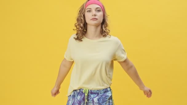 An attractive young athletic couple man and woman in sportswear are shooting video doing exercises and having fun together isolated over a yellow background in studio - Felvétel, videó