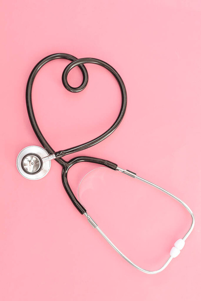 Stethoscope in the shape of heart on pink background Medicine concept, symbolic association with love, cardiology - Fotó, kép