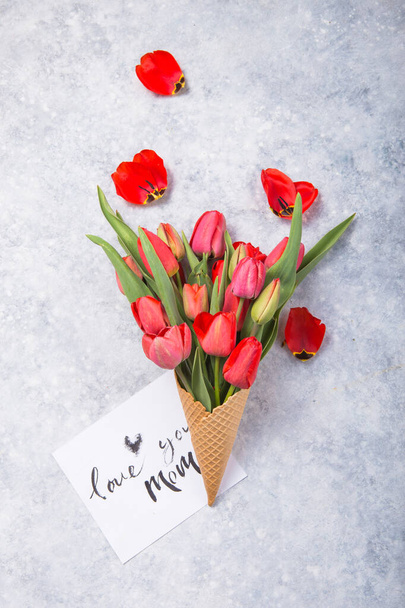 Ice cream of red  tulip flowers in waffle cone with card Love you mom  on concrete  table top view in flat lay style. - Fotografie, Obrázek