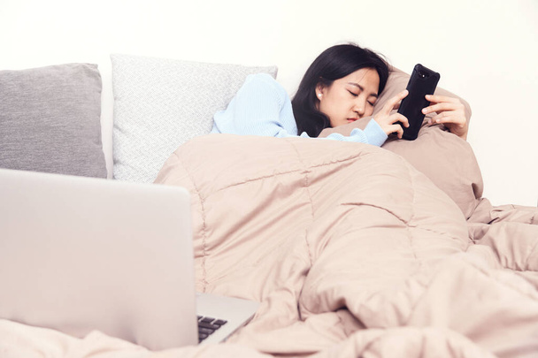若いアジアの女性はベッドの上でリラックス。寝室で携帯電話を使う - 写真・画像