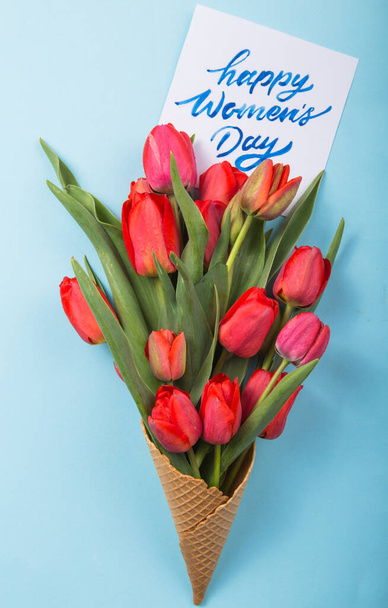 czerwone piękne tulipany w rożku lodowym z kartą Dzień Kobiet na konkretnym tle. Pomysł na prezent kwiatowy. nastrój wiosenny - Zdjęcie, obraz