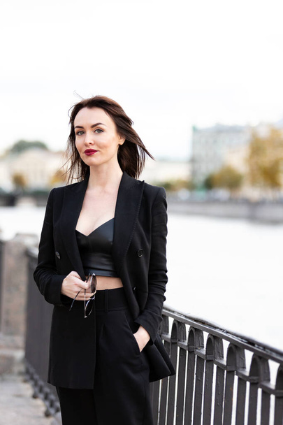 Beautiful woman in black pantsuit walks on promenade in Saint-Petersburg - Фото, зображення