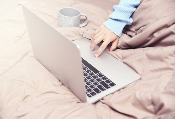 Asiatin mit Laptop und einer Tasse Kaffee auf dem Bett. Arbeiten zu Hause im Schlafzimmer - Foto, Bild