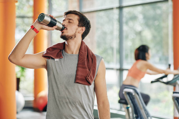 Thirsty sportsman with towel on shoulder drinking water after training in gym - Fotoğraf, Görsel