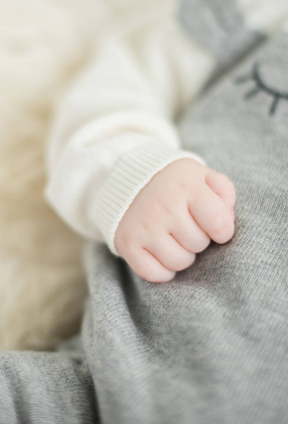 A beautiful soft delicate warm young baby hand photographed with a shallow depth of field. gentle calm colours and feel. baby care and well being. babies hands on a cream fur rug. - 写真・画像