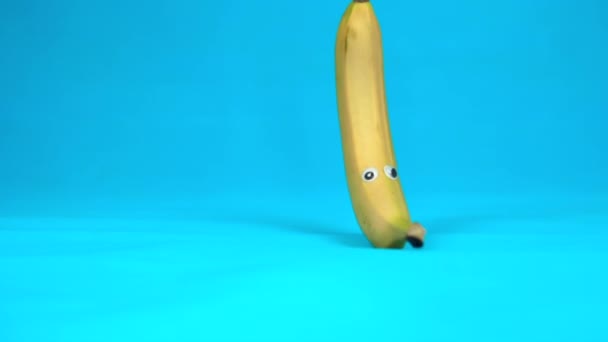 Μπανάνα με μάτια κυλάει αργά. Μπανάνα με ρολά σε μπλε φόντο. Αργή κίνηση. - Πλάνα, βίντεο