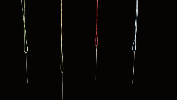 Four needles hanging with green yellow red and blue threads on a black background - Foto, imagen