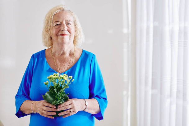 Retrato de una mujer mayor sonriente de pie con un jarro de flores en las manos - Foto, imagen