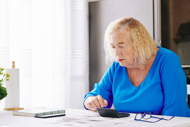 Ηλικιωμένη γυναίκα κάνει υπολογισμούς κατά τον έλεγχο των λογαριασμών της - Φωτογραφία, εικόνα